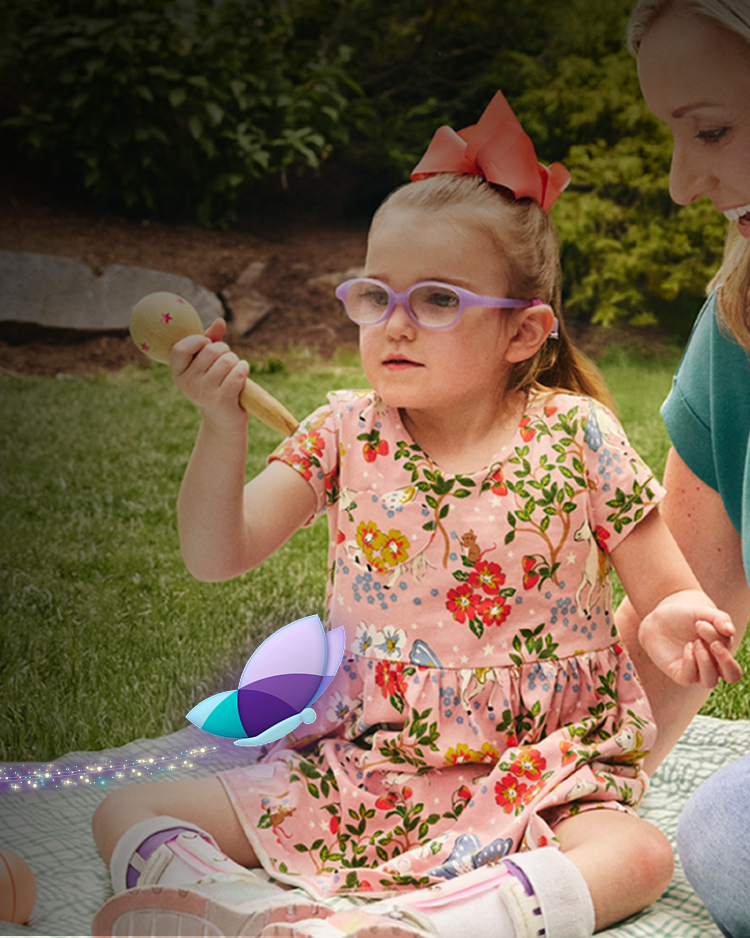 Niña y persona adulta sentadas juntas sobre una manta al aire libre, jugando con juguetes en un jardín.